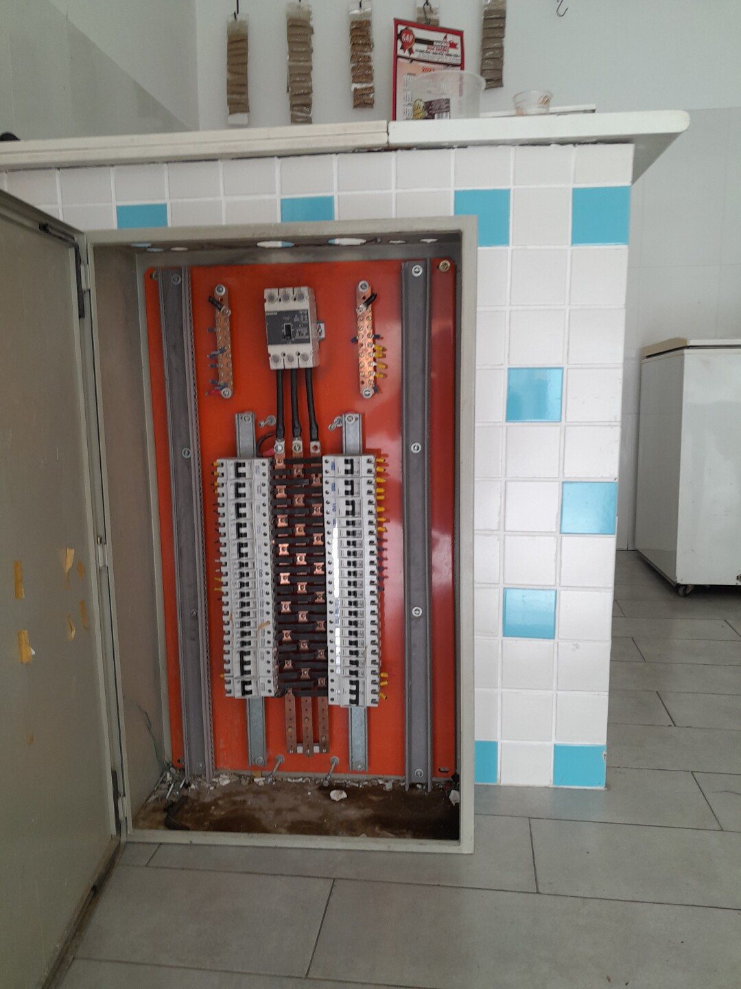 Quadro de distribuição aberto em parede de azulejo, com disjuntores e barramento